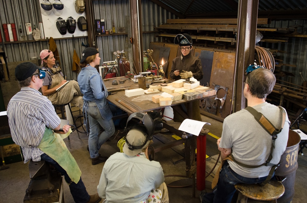 Six people standing around a table of materials ready to work on metalwork